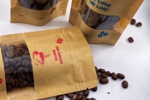 Three brown paper coffee bags with different designs printed on them and loose coffee beans scattered around them.