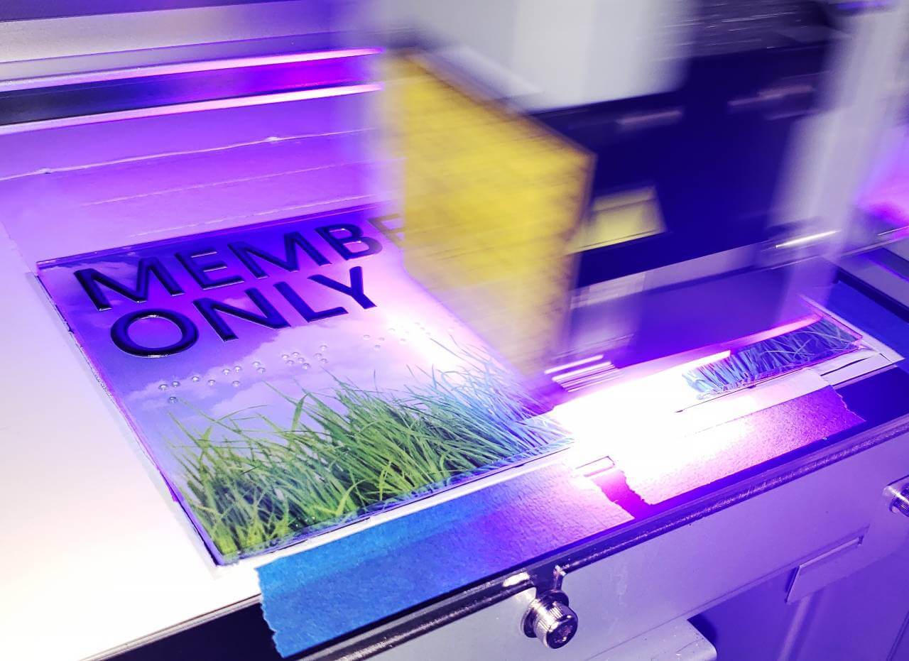 image of large format printer printing a colorful sign with grass on it. sign also has braille on it
