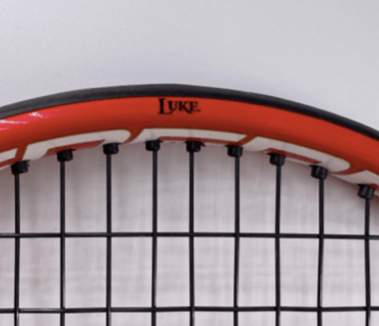 Red tennis racquet with the name “LUKE” printed on it in black ink and a bold font.