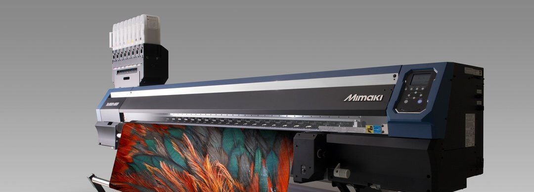 The image features a high-end Mimaki Tx300P-1800 wide format printer, known for its textile printing capabilities. This printer is designed to print directly onto fabrics with high precision and vibrant colors, making it suitable for producing detailed and colorful fabric prints. Such printers are widely used in the fashion and textile industries for creating custom garments, decorative fabrics, and soft signage. The displayed model highlights its robust construction and advanced technology, showcasing a fabric with a vividly printed design emerging from the printer, demonstrating its ability to handle complex, colorful patterns efficiently.